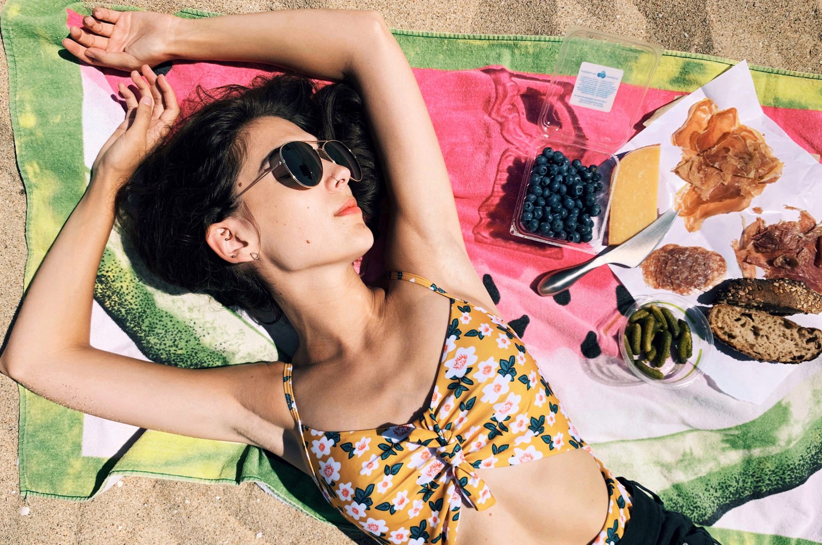 Lying on a beach towel in sunglasses beside a picnic spread